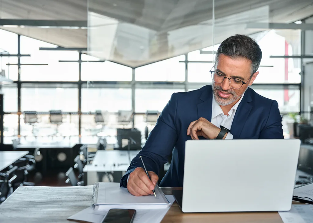 Ultimate Beneficial Owner of a business works on laptop and writes notes